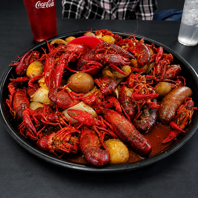 A large platter of boiled crawfish, potatoes, onions, and sausage in a rich sauce.