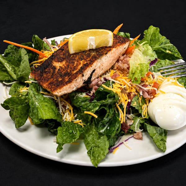 Blackened salmon salad with mixed greens, shredded cheese, bacon bits, and hard-boiled eggs.
