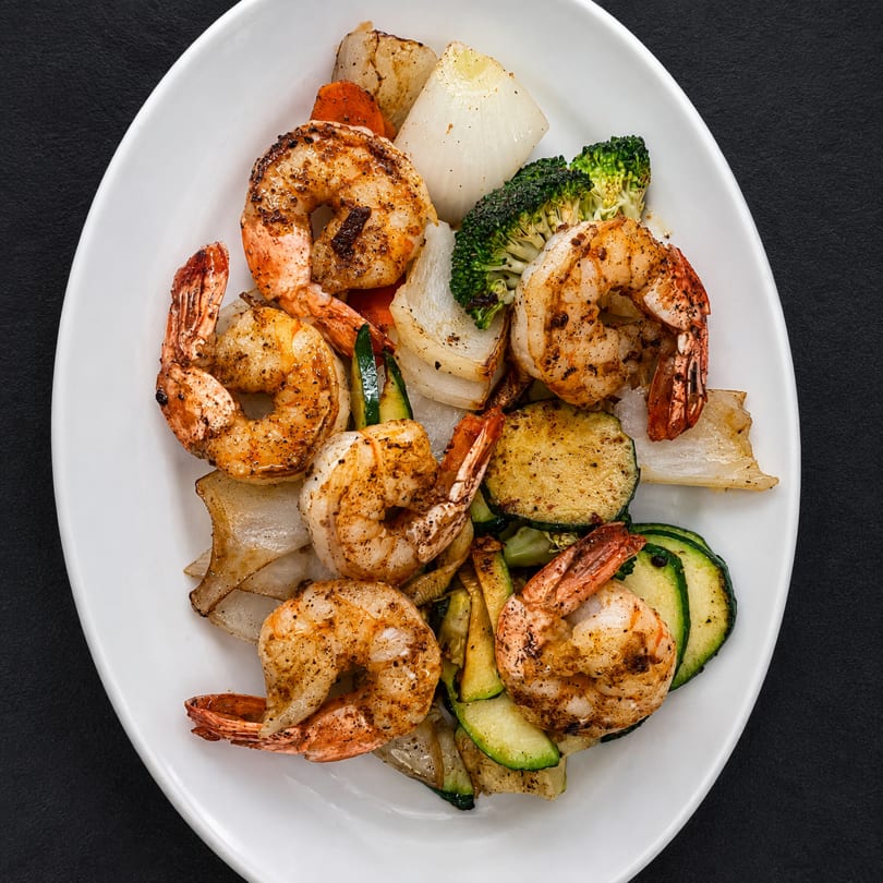 Grilled shrimp and mixed vegetables including zucchini, broccoli, onions, and carrots on a white plate.