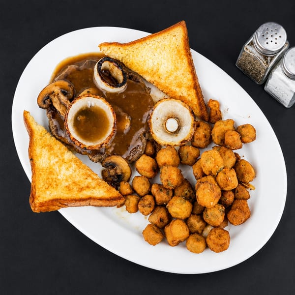 A white plate with steak, gravy, grilled onions, mushrooms, fried mushrooms, and toast.
