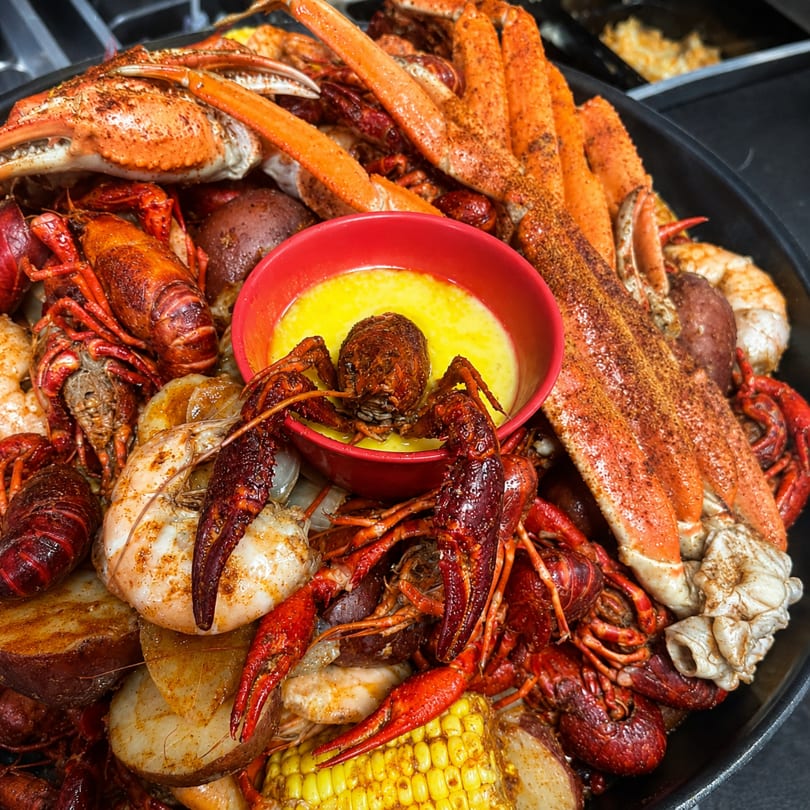 A seafood boil with crab legs, crawfish, shrimp, potatoes, corn, and a bowl of butter.