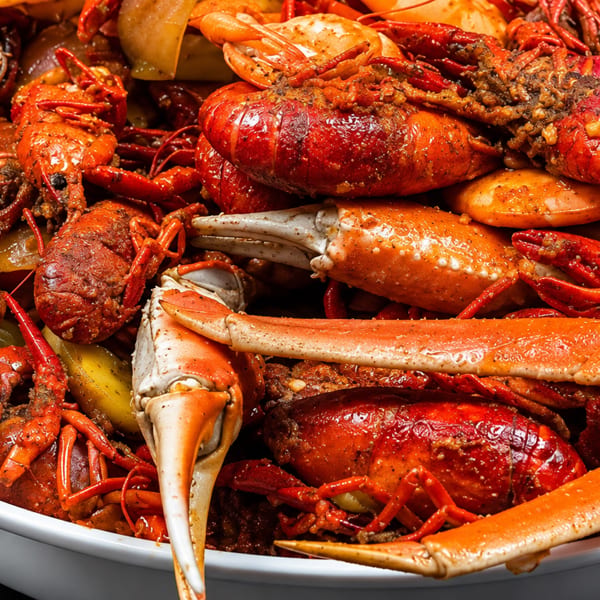 A large white bowl overflowing with seasoned red crawfish, crab legs, and potatoes.
