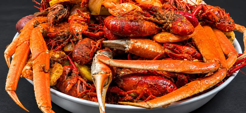 A large white bowl overflowing with seasoned red crawfish, crab legs, and potatoes.