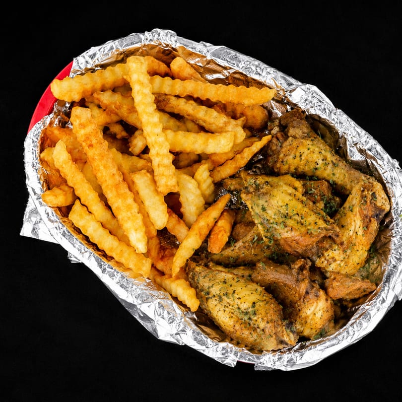 Crispy crinkle-cut fries and seasoned chicken wings in a foil-lined takeout container.